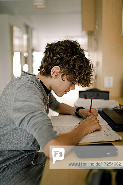Junge schreibt in Buch  während er am Tisch sitzend Hausaufgaben macht