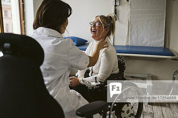 Female doctor checking pulse of smiling disabled patient at medical clinic