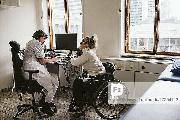 In voller Länge von weiblichen Arzt schriftlich Rezept für behinderte Patienten  während am Schreibtisch sitzen