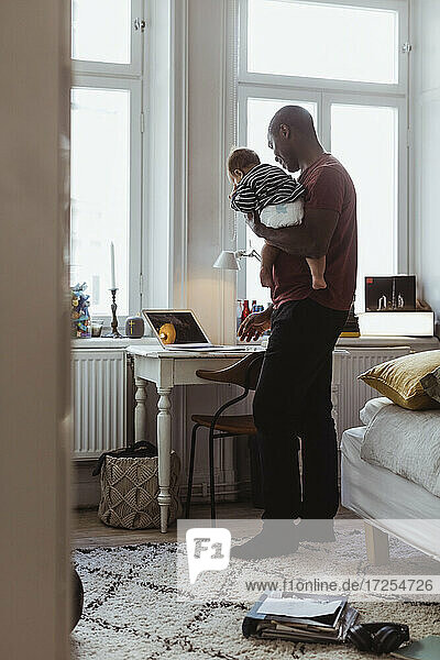 Geschäftsmann trägt Baby Junge  während mit Laptop im Büro zu Hause