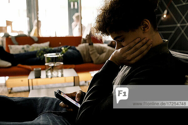 Teenager-Junge mit Smartphone  während der Vater auf dem Sofa im Wohnzimmer liegt