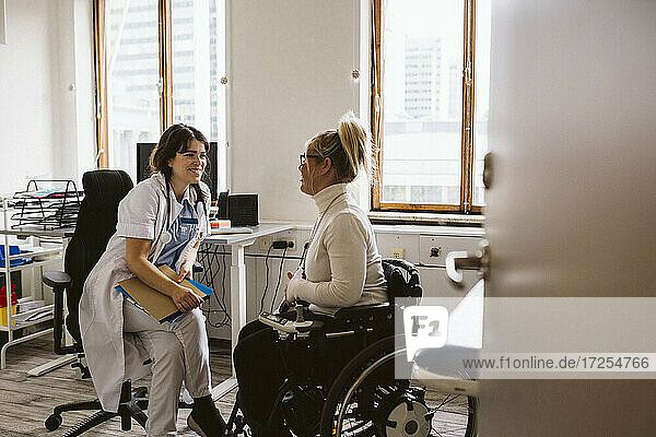 Lächelnder weiblicher medizinischer Experte  der eine behinderte Frau im Gespräch in einer medizinischen Klinik betrachtet