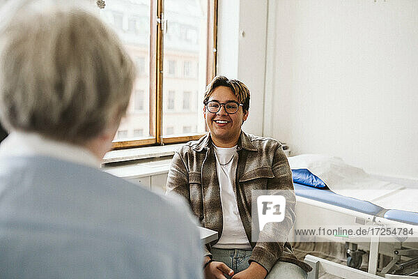 Lächelnde junge männliche Patient Blick auf ältere weibliche Arzt in der medizinischen Klinik