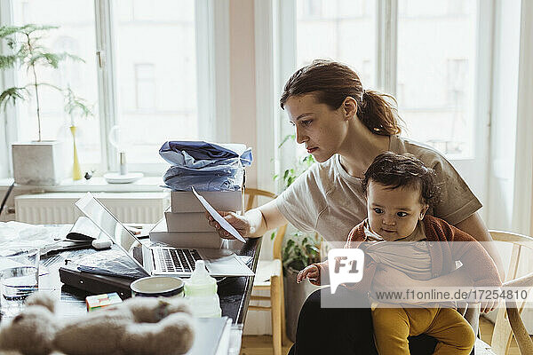 Geschäftsfrau liest Dokument  während sie mit Baby Junge im Wohnzimmer sitzt