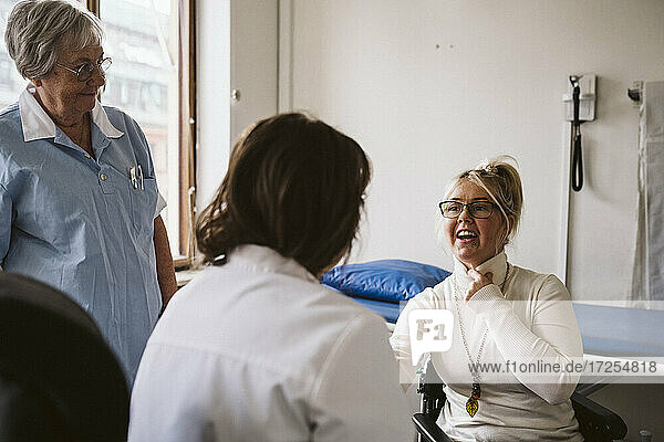 Senior female nurse looking at disabled woman consulting with doctor at medical clinic
