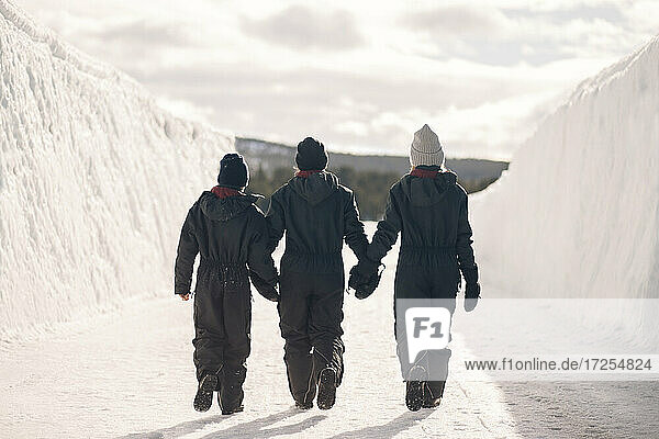 Full length rear view of mother holding hands of son and daughter while walking on snow during winter