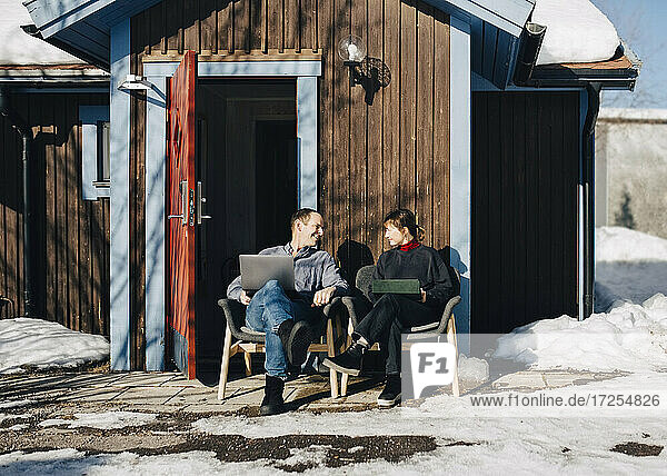 Geschäftsmann und Geschäftsfrau diskutieren  während sie vor einem Ferienhaus im Winter sitzen