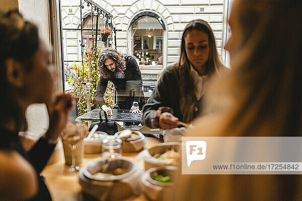 Multi-ethnischen weiblichen Freunde mit Essen im Restaurant  während Kellner Reinigung Tabelle außerhalb