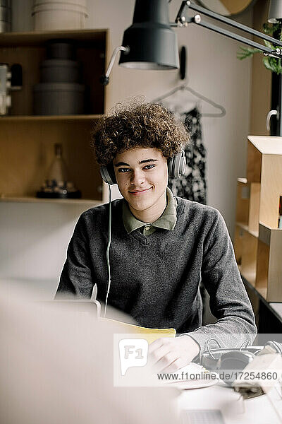 Porträt von lächelnden lockiges Haar Junge trägt Kopfhörer sitzen am Schreibtisch
