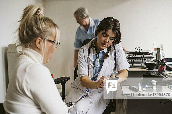 Weibliche Mitarbeiterin im Gesundheitswesen diskutiert mit einem Patienten über ein Glaukomgerät in einer medizinischen Klinik