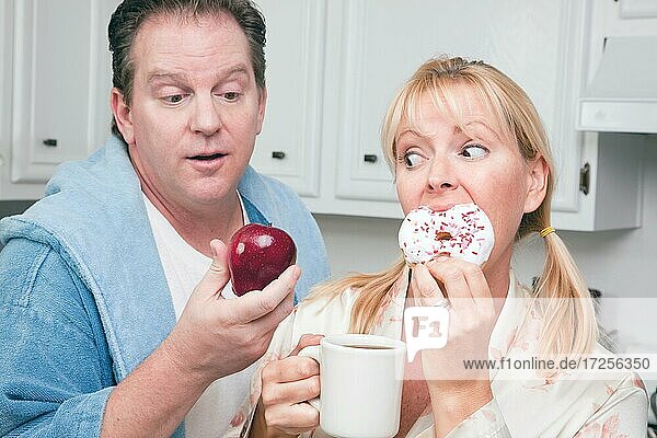 Couple in kitchen eating donut and coffee or healthy fruit