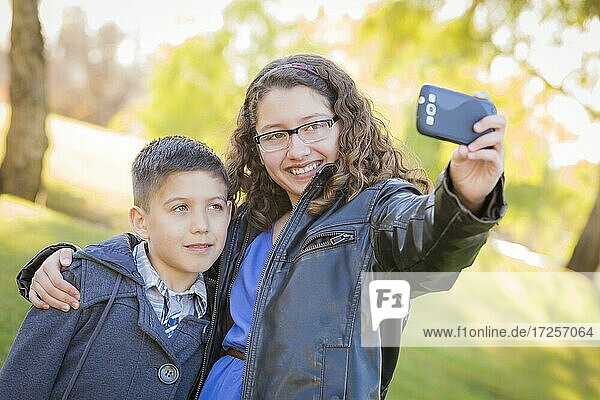 Brother and sister taking cell phone picture of themselves outdoors at the park