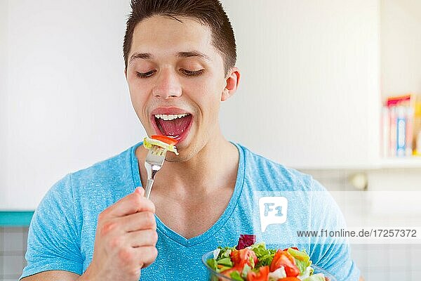 Junger Mann ißt essen Salat in der Küche gesunde Ernährung vegan lachen in Deutschland