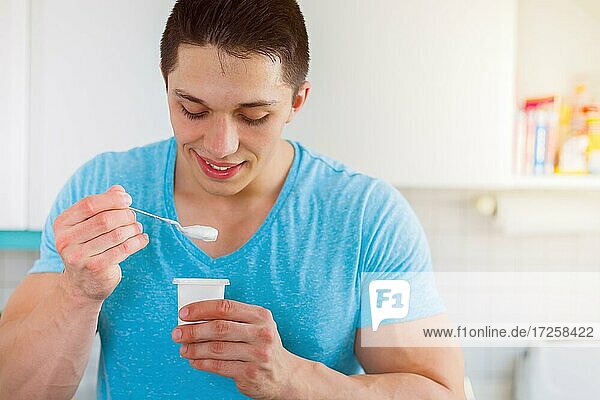 Junger Mann ißt essen Joghurt in der Küche gesunde Ernährung Frühstück lachen in Deutschland
