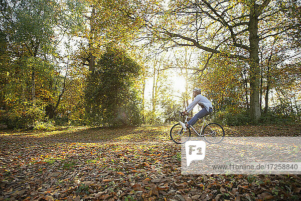Sorglose junge Frau fährt mit dem Fahrrad durch Herbstlaub im Park