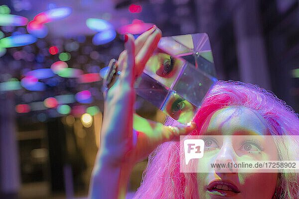 Frau mit rosa Haaren blickt auf einen dimensionalen Kristallwürfel