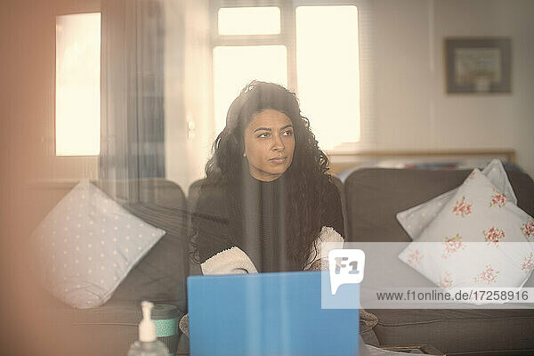 Frau mit Kopfhörer arbeiten von zu Hause am Laptop auf dem Sofa