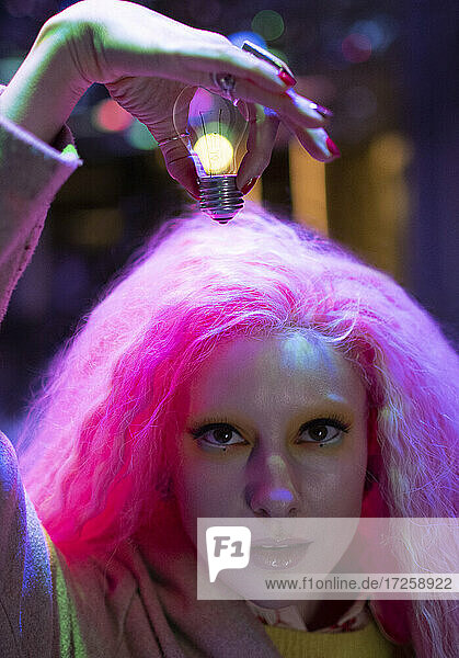 Porträt kühle Frau mit rosa Haar hält Glühbirne über Kopf