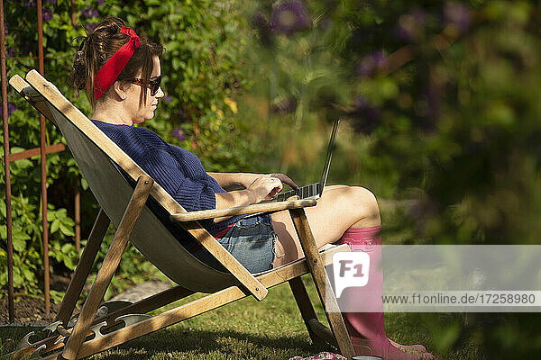 Frau arbeitet am Laptop in Rasen Stuhl in sonnigen Sommergarten