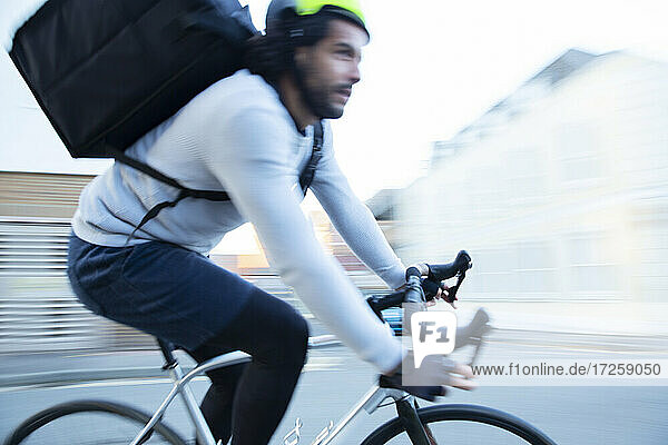 Männlicher Fahrradkurier  der Lebensmittel ausliefert  fährt auf der Straße zu schnell