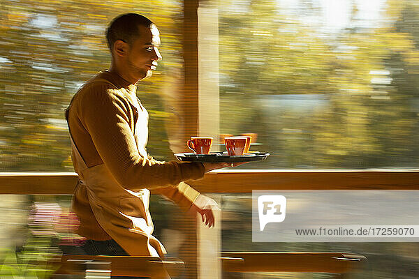 Männliche Barista trägt Tablett von Kaffeetassen entlang Herbst Café Fenster