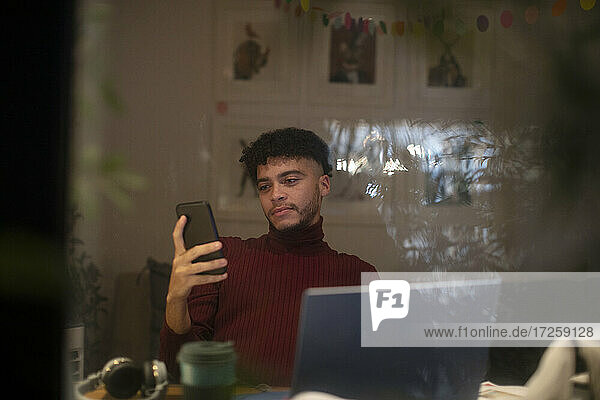 Junger Mann arbeitet von zu Hause aus mit Smartphone und Laptop