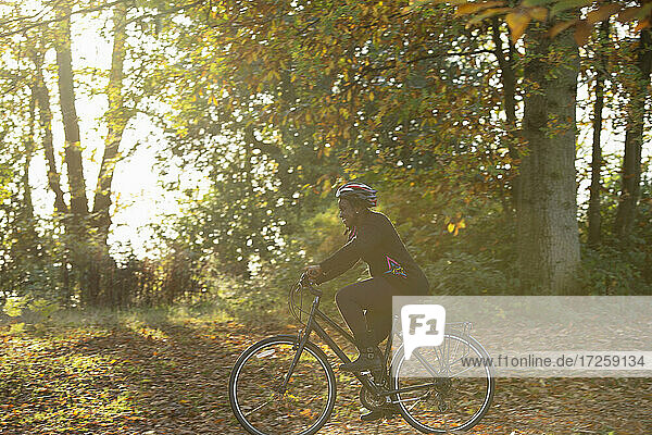Glückliche Frau Fahrradfahren unter Herbstlaub in sonnigen Park