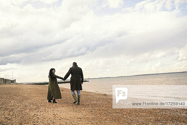 Couple in winter coats holding hands walking on ocean beach
