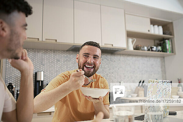 Happy gay male couple eating in kitchen