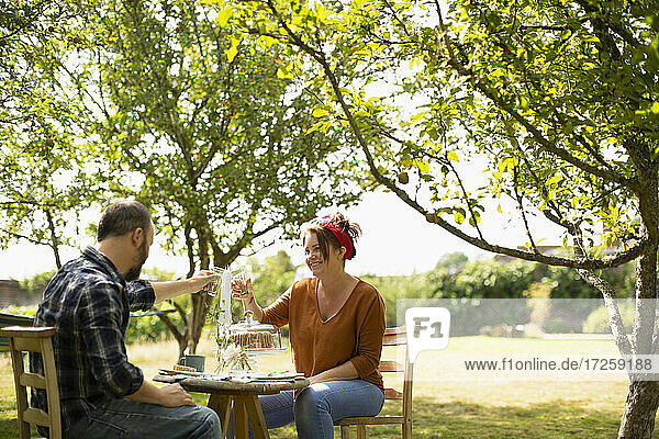 Glückliches Paar Toasting Wassergläser am Tisch in sonnigen Sommergarten