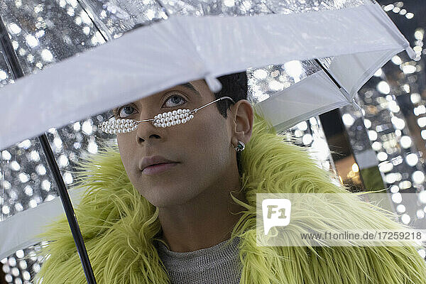 Porträt modischer junger Mann in Federboa unter Regenschirm