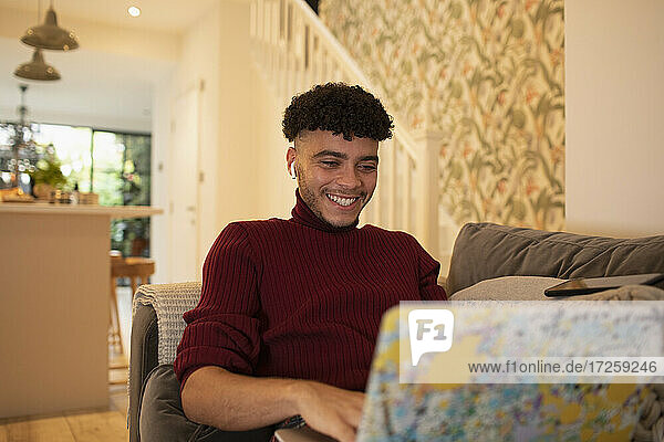 Glücklicher junger Mann mit Laptop auf dem Sofa
