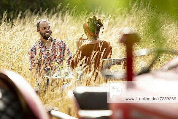Glückliches Paar am Tisch hinter Traktor in sonnigen Sommer hohes Gras