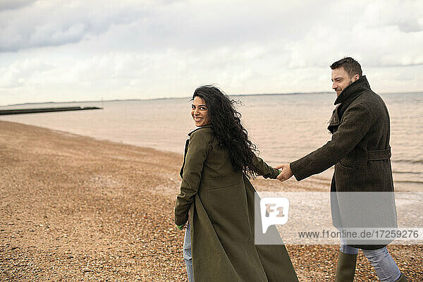Porträt glückliches Paar in Wintermäntel halten Hände auf Ozean Strand