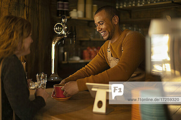Freundlicher Barista serviert Kaffee an aufgeregte Frau am Café-Tresen