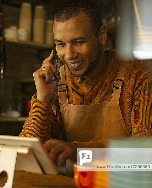 Lächelnder männlicher Barista  der eine Bestellung per Telefon am digitalen Tablet im Café aufnimmt