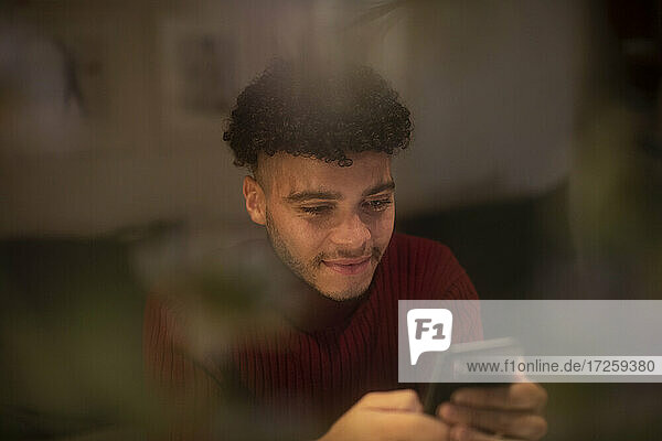 Lächelnder junger Mann mit Smartphone im Fenster