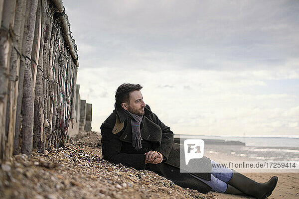 Gelassener Mann im Wintermantel entspannt am Strand