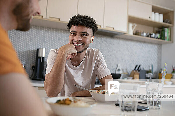 Smiling gay male couple talking and eating in kitchen