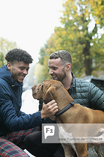 Happy gay male couple petting dog on street