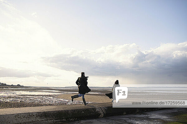 Paar in Wintermäntel laufen auf sonnigen Ozean Strand Steg