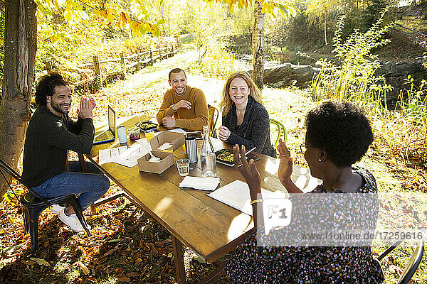 Glückliche Geschäftsleute essen und arbeiten am Tisch im sonnigen Herbst Park