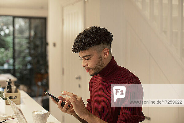 Junger Mann mit Smartphone in der Küche