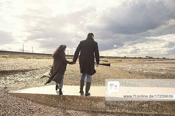 Couple in winter coats holding hands walking on sunny beach