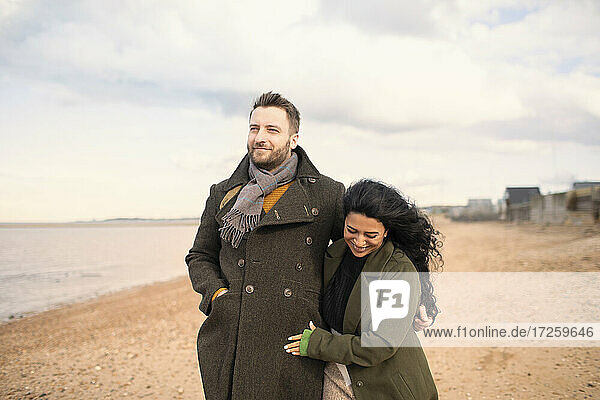 Happy couple in winter coats walking on ocean beach