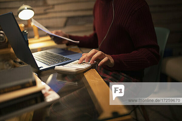 Junger Mann mit Taschenrechner beim Bezahlen von Rechnungen am Laptop im Home Office
