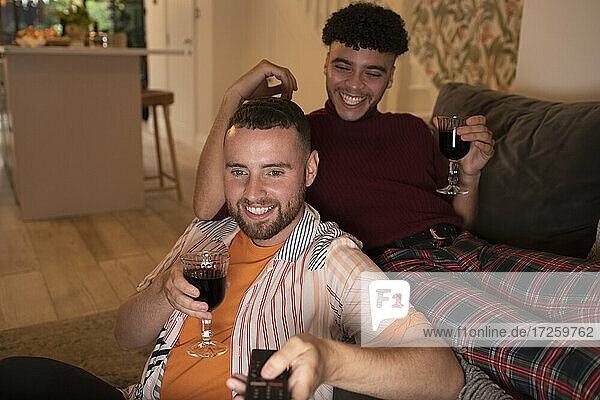 Glückliches schwules männliches Paar trinkt Wein und sieht auf dem Sofa fern
