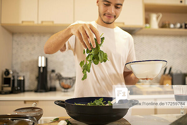 Junger Mann kocht mit frischem Spinat in der Küche