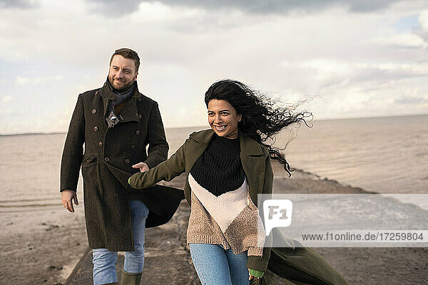 Glückliches Paar in Wintermänteln  die sich auf dem Bootssteg an den Händen halten