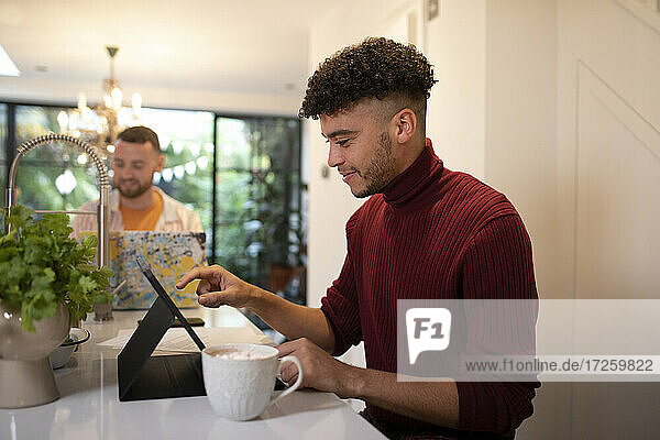 Junger Mann arbeitet von zu Hause aus am digitalen Tablet in der Küche